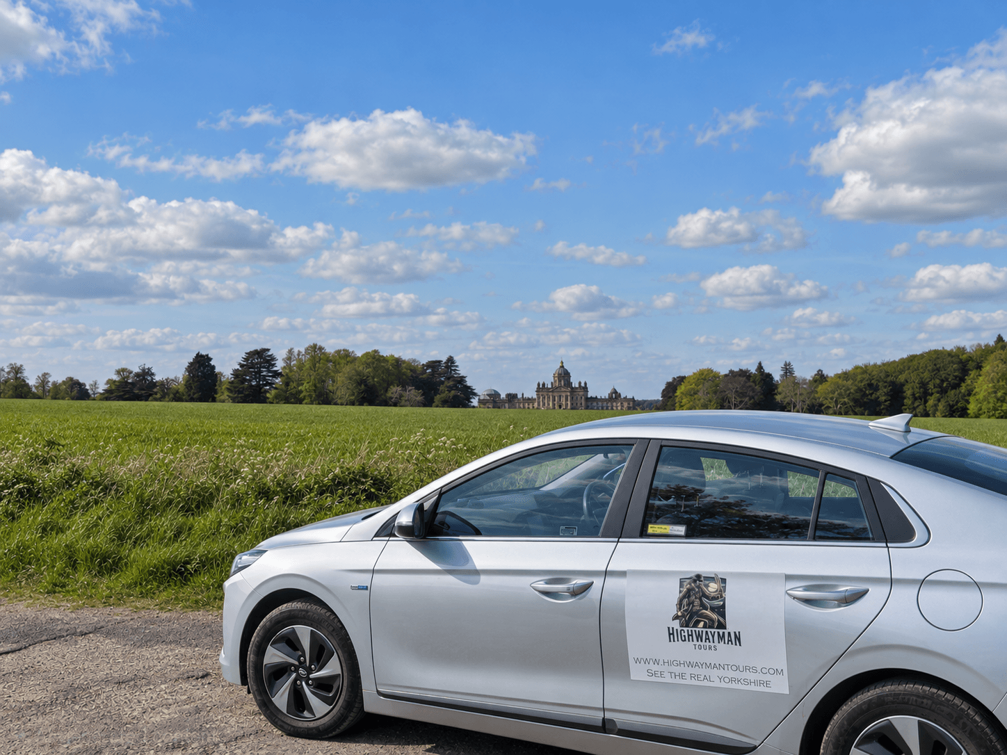 Highwayman Tours' silver Hyundai Ioniq parked in the Yorkshire countryside with Castle Howard in the background